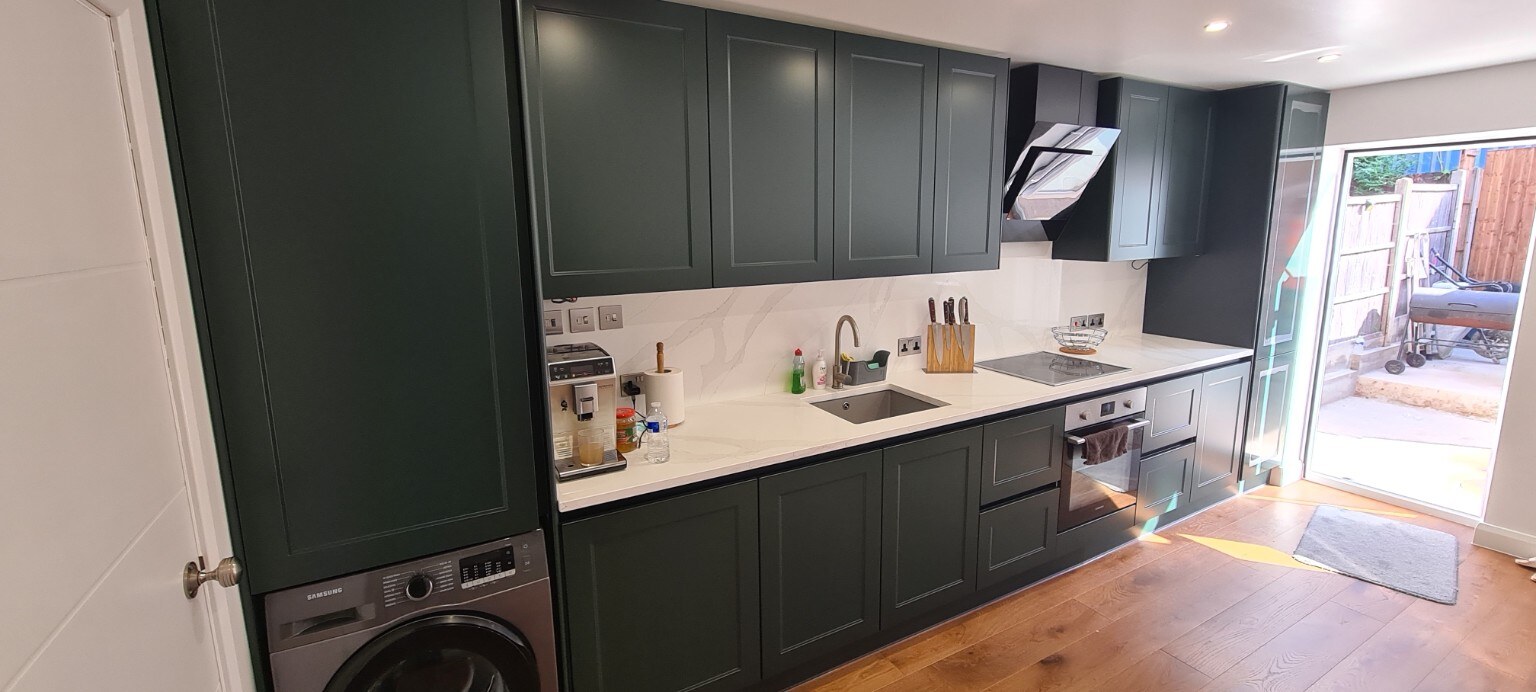 Completed deep-green Shaker kitchen with pale marble-effect splashback and integrated appliances