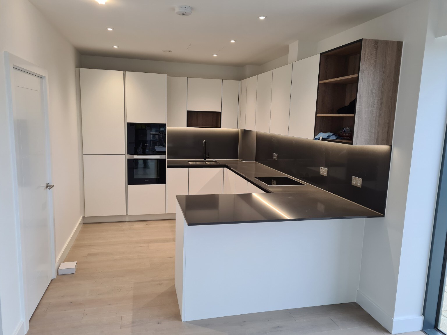 Completed white handleless kitchen with dark worktops, timber display cabinetry and peninsula